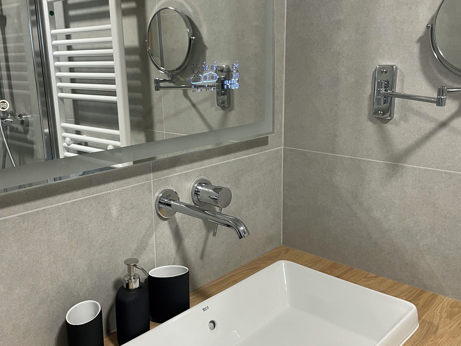 A modern bathroom with a white sink, two black soap dispensers, a mirror, and a towel rack.