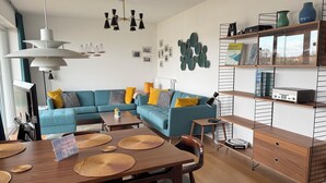 Una sala de estar moderna con un sofá azul, una mesa de centro de madera y un comedor con una mesa y sillas de madera.