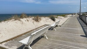 Una pasarela de madera con bancos a lo largo de una playa arenosa, que se extiende hasta el océano.