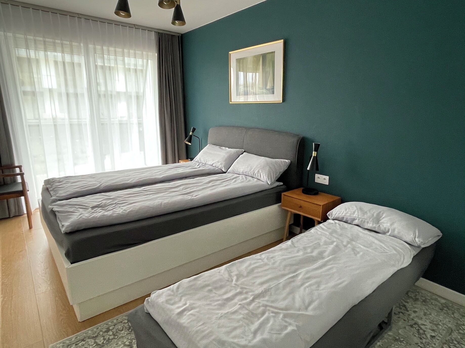 A hotel room with two beds, a nightstand, a lamp, a framed picture, and a window with curtains.