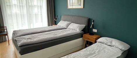 A hotel room with two beds, a nightstand, a lamp, a framed picture, and a window with curtains.