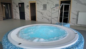 Un jacuzzi con borde de azulejos, rodeado por una habitación con paredes de mármol y suelo de baldosas.