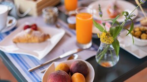 Uma mesa de café da manhã com uma travessa de frutas, um copo de suco de laranja e um pequeno vaso com flores.