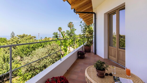 Varanda com vista para o mar, plantas em vasos e uma mesa com bebidas.