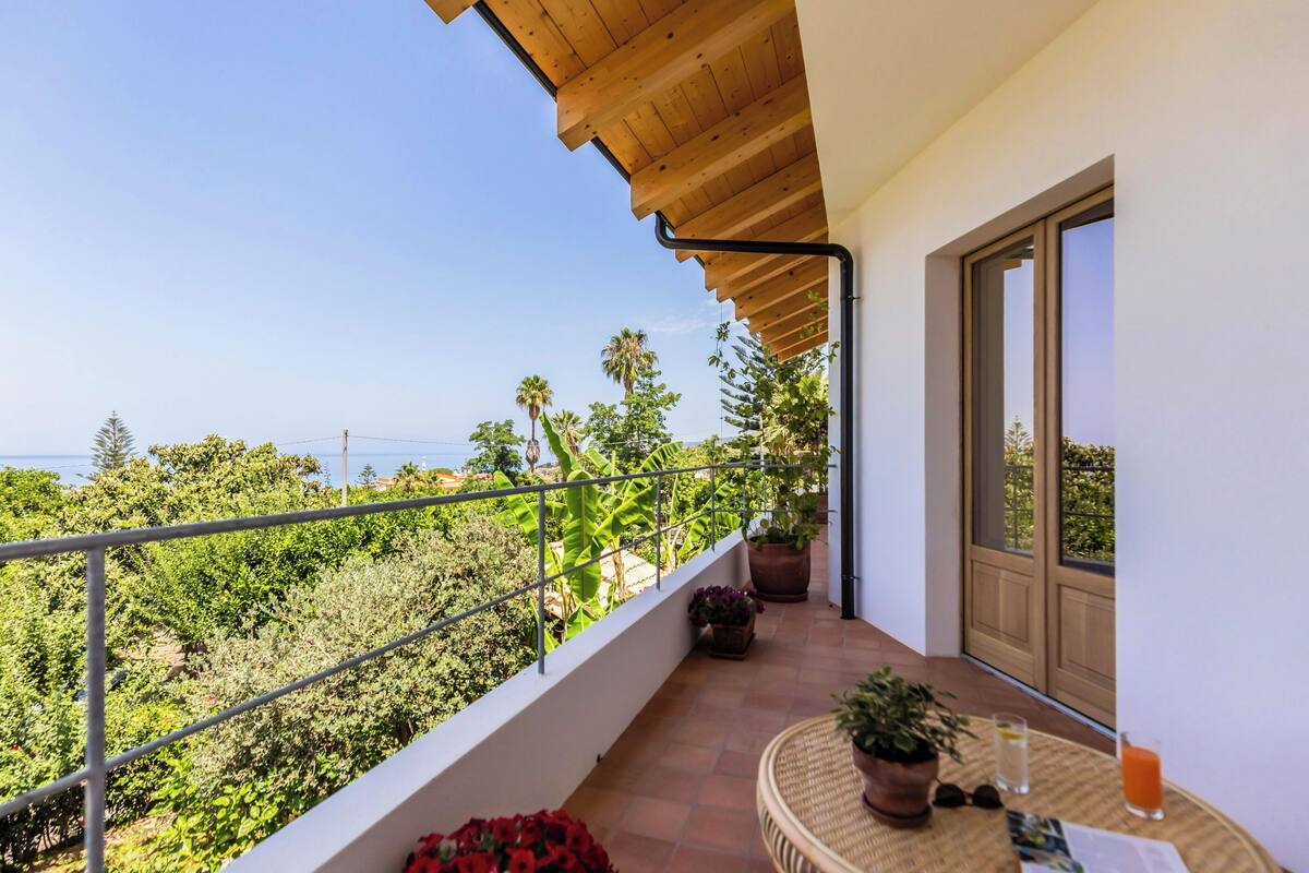 A balcony with a view of the sea, potted plants, and a table with drinks.