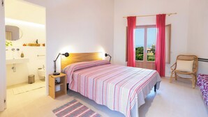 Quarto com cama, mesa de cabeceira, luminária e janela com cortinas.