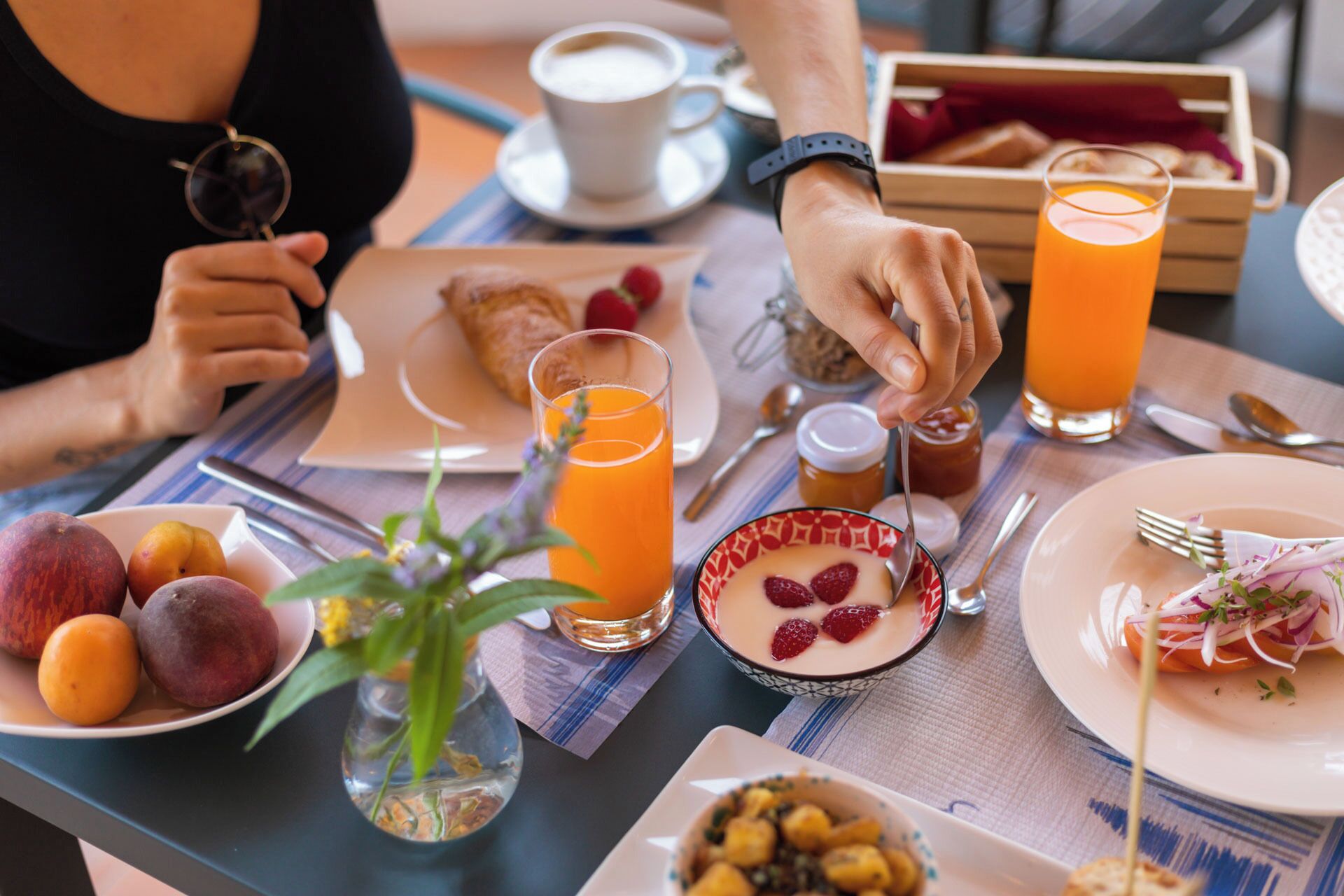 Mesa de café da manhã com diversas opções de alimentos e bebidas, incluindo frutas, um croissant e suco de laranja.