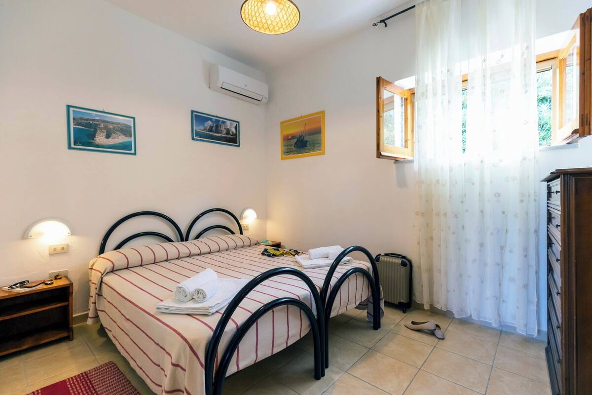 A bedroom with two beds, a nightstand, a radiator, and a window with curtains.