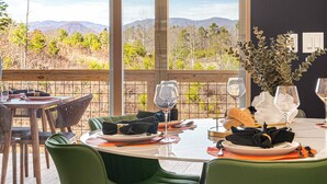 A dining area with tables set for two, featuring green upholstered chairs, white tablecloths, and a view of a mountainous landscape through large windows. - Game Room + Spa Stay, Sauna, Hot Tub, Dogs OK (Leicester)
