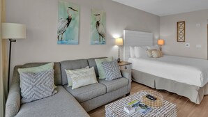 A well-lit room with a grey sofa, a bed, and two wall-mounted paintings of birds. - Serene 4th Floor Elation Condo: Golf Course and Foliage Views! King Bed, Sleeper Sofa, Kitchenette for Your Convenience at Sandestin Golf and Beach Resort!! (Miramar Beach)
