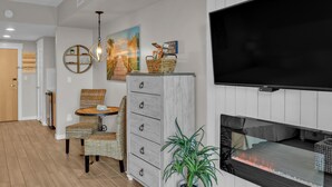 A modern living room with a flat-screen TV, a fireplace, wicker furniture, and decorative items on the wall. - Serene 4th Floor Elation Condo: Golf Course and Foliage Views! King Bed, Sleeper Sofa, Kitchenette for Your Convenience at Sandestin Golf and Beach Resort!! (Miramar Beach)