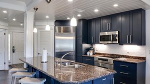 Una cocina moderna con armarios azul oscuro, electrodomésticos de acero inoxidable, encimera de granito e iluminación colgante.