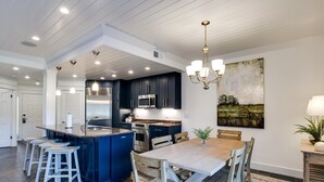 Una cocina moderna con armarios oscuros, una isla central, taburetes de bar y una mesa de comedor con sillas.