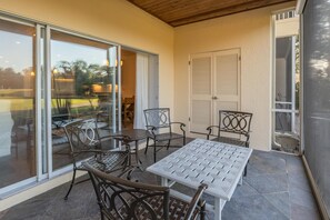 Ein überdachter Patio-Bereich mit Tisch und Stühlen, eine Glasschiebetür zu einem Garten und eine weiße Tür mit Fensterläden.