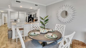 Zona pranzo con tavolo rotondo, sedie bianche e uno specchio decorativo al muro.