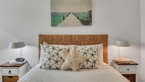 Camera da letto con testiera in legno, cuscino a forma di stella marina, quadro raffigurante un molo e lampade da comodino.