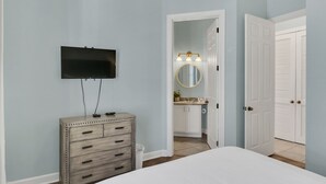 A bedroom with a bed, dresser, TV, and a bathroom visible through an open door. - Spacious 3-Bedroom Retreat with Lake Views (Miramar Beach)