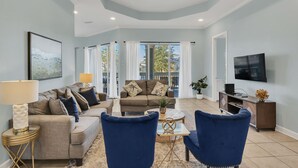 A spacious living room with a sofa set, two blue armchairs, a coffee table, and a TV mounted on the wall. - Spacious 3-Bedroom Retreat with Lake Views (Miramar Beach)