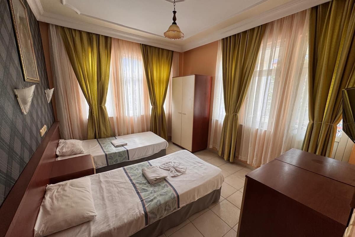 Habitación de hotel con dos camas individuales, un armario y un escritorio.