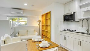 A modern kitchen with white cabinets, a microwave, and a gas stove. There is a dining area with a wooden table and white chairs. - 3 Mi to Angel Stadium: Cozy Studio w/ Patio! (Santa Ana)