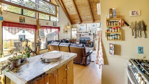 Eine gemütliche Küche mit Holzbalkendecke, einem Essbereich mit einer Couch und Blick ins Freie durch große Fenster.