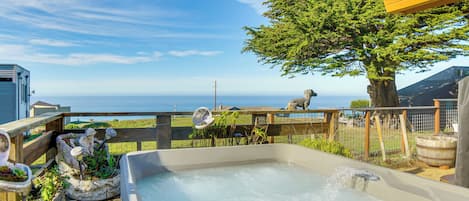 A hot tub with a view of the ocean, surrounded by potted plants and a wooden deck.