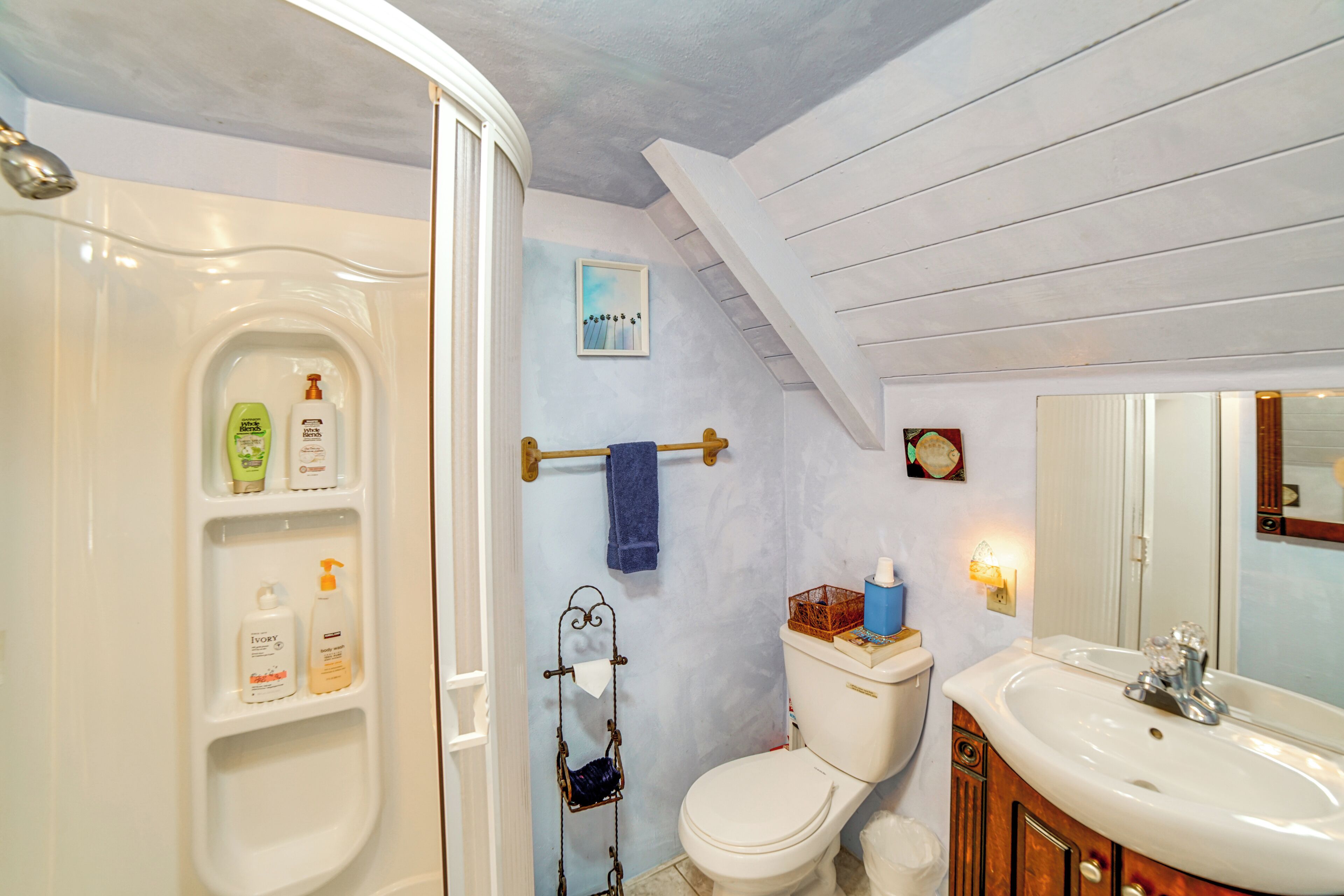 Casa de banho com uma banheira branca, sanita e lavatório. Há produtos de higiene pessoal na parede e um porta-toalhas.