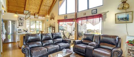 A spacious living room with leather sofas, a wooden coffee table, and large windows offering a view of the outdoors.