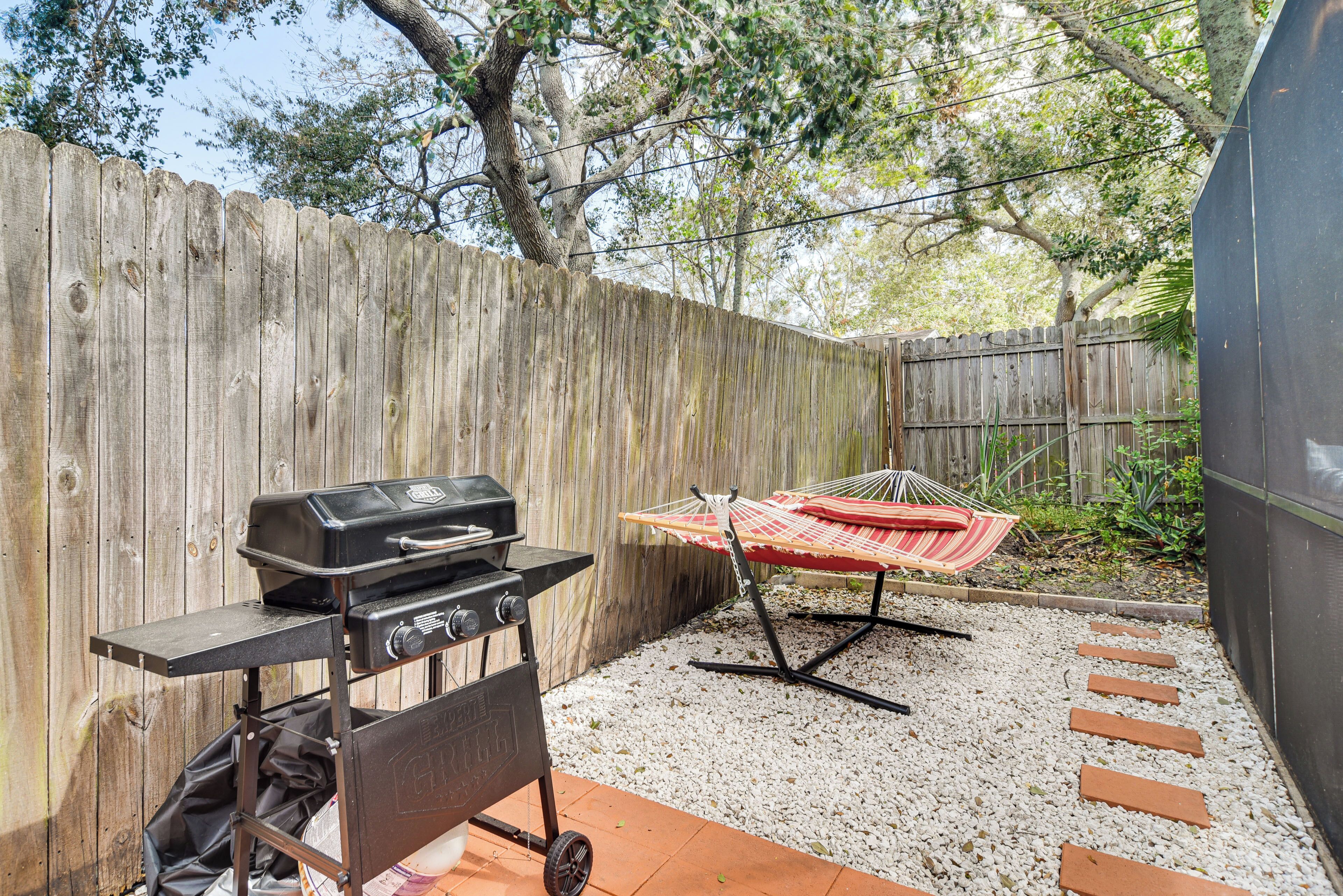 A backyard with a wooden fence, a grill, a hammock, and a gravel path.