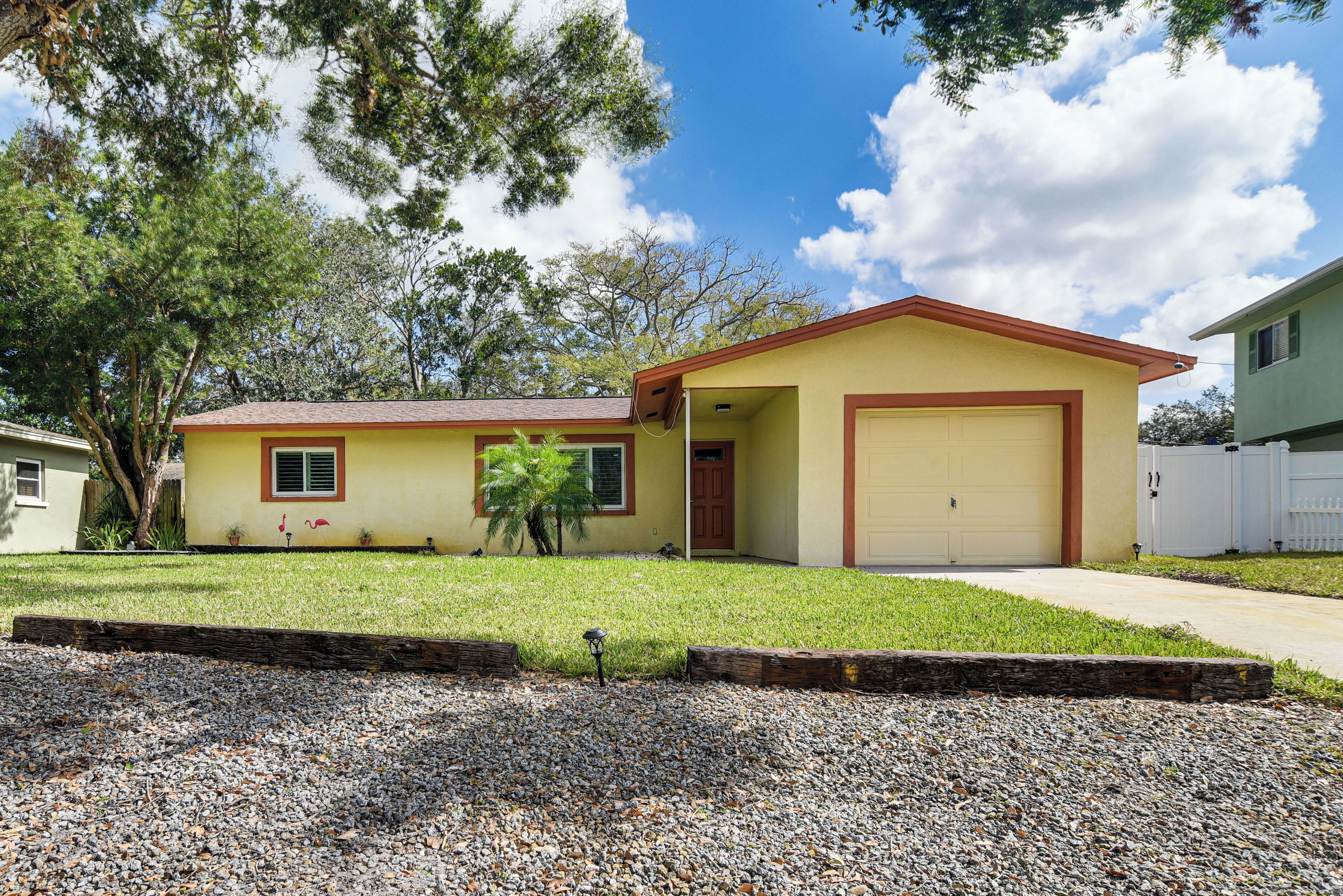 A single-story house with a garage, a well-maintained lawn, and a gravel driveway.