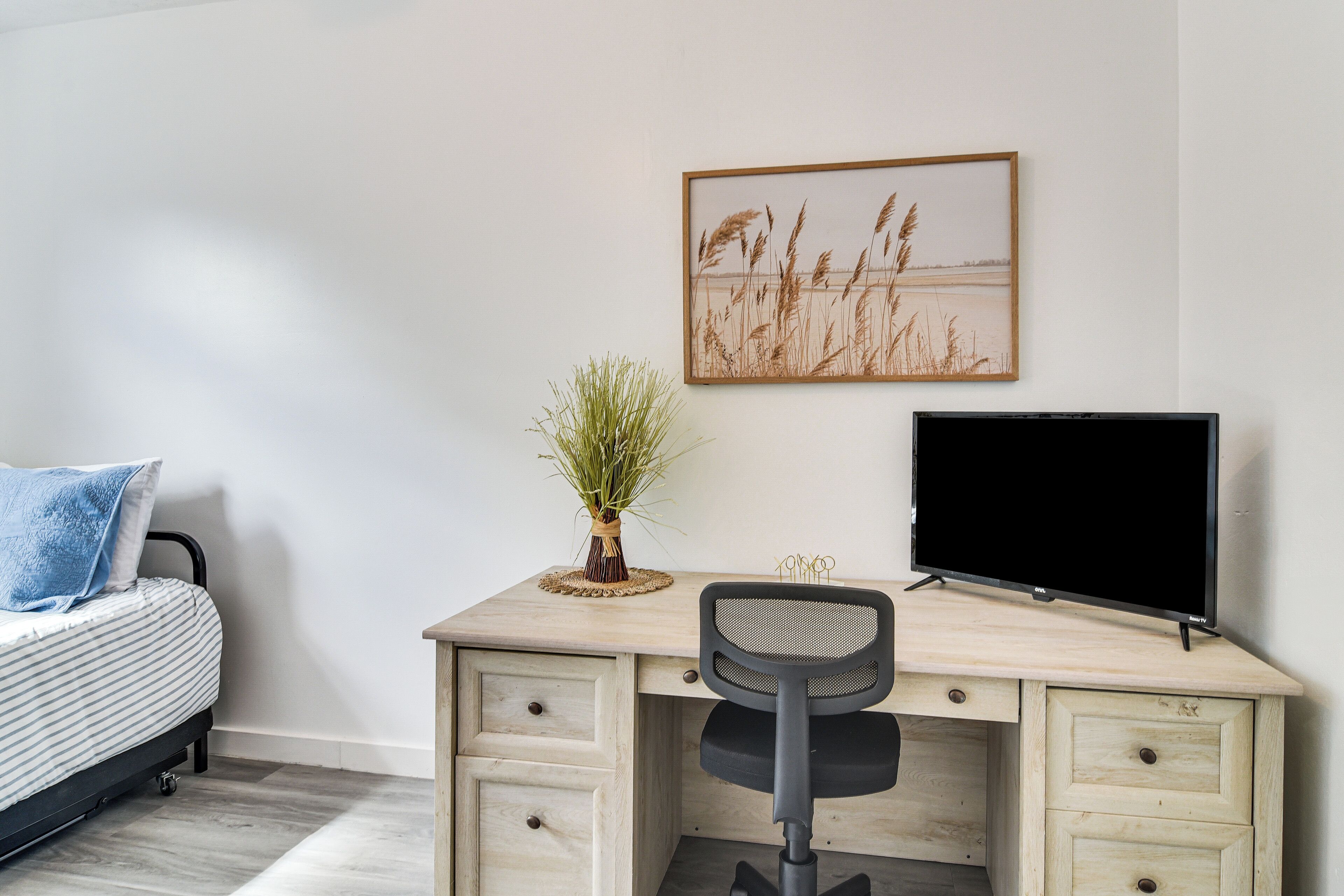 Une chambre à coucher comprenant un lit, un bureau avec une chaise, un téléviseur et un tableau accroché au mur.