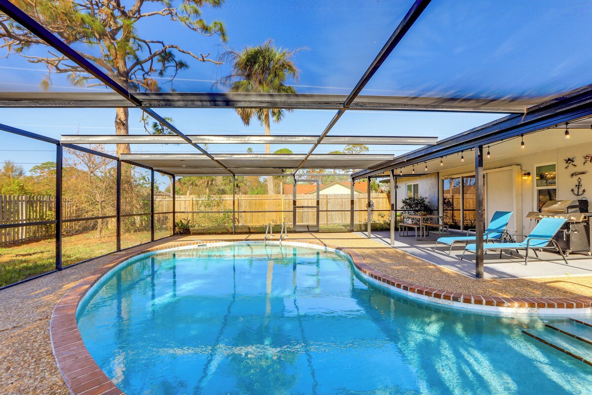 Una piscina con cerramiento de vidrio, rodeada por un patio con sillas de descanso y una parrilla.