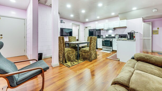 A modern kitchen with white cabinets, a dining area with patterned chairs, and a wooden floor.