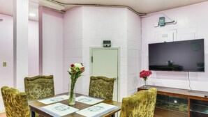 A dining area with a table set for four, surrounded by patterned chairs, a vase with flowers, and a flat-screen TV mounted on the wall.