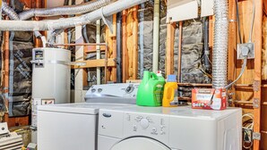 A front-loading washer and dryer in a utility room with exposed wooden framing and insulation.