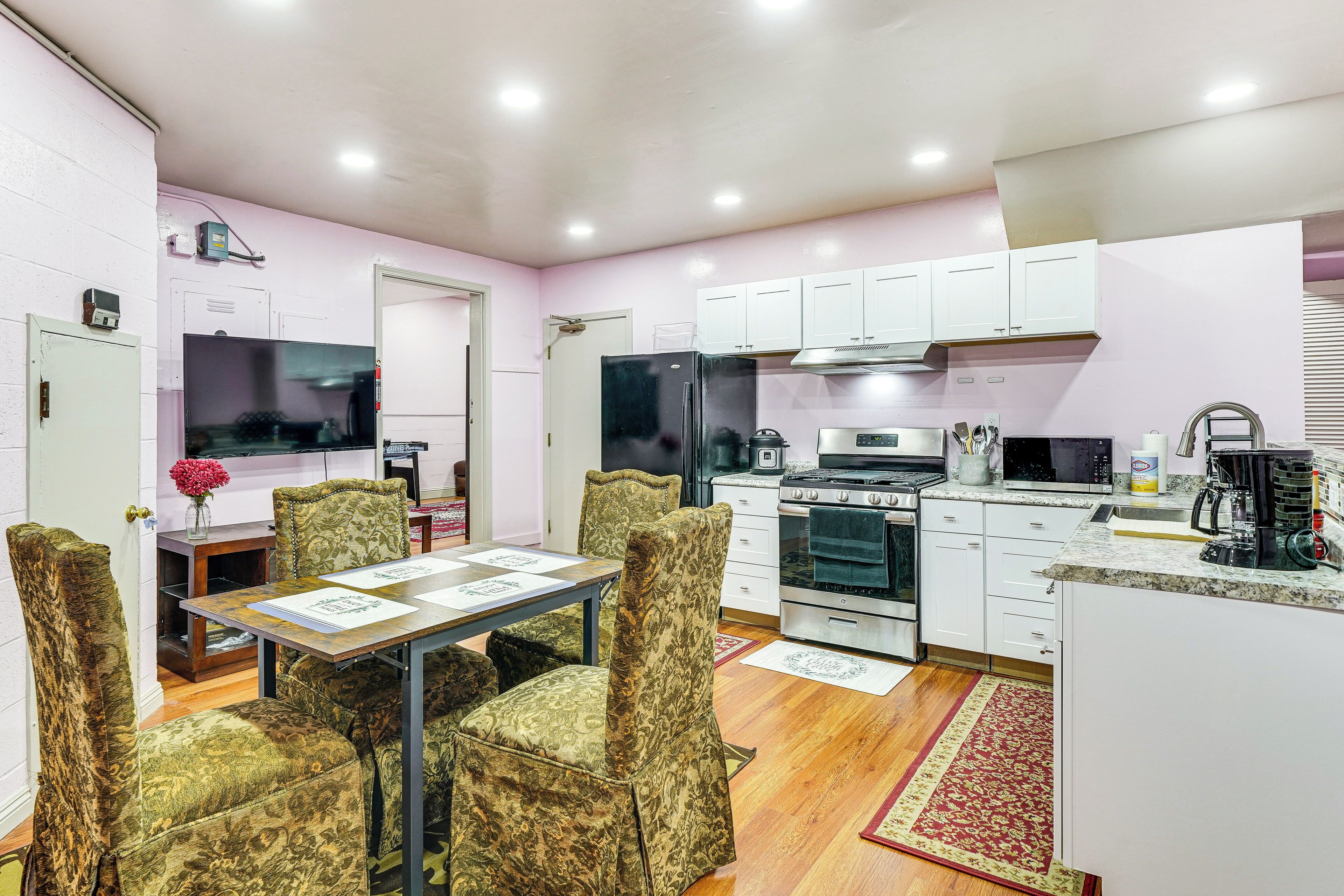 A compact kitchen with white cabinets, a refrigerator, stove, microwave, and a dining area with patterned chairs and a table.