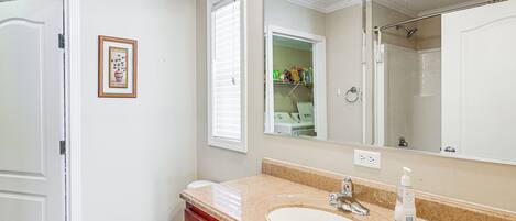 A bathroom with a white sink, vanity, and mirror. There is a framed picture on the wall and a toilet visible.