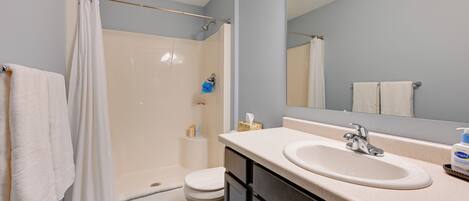 A bathroom with a shower, toilet, sink, and mirror.