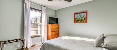 Un dormitorio con cama, cómoda, televisor, un cuadro y ventilador de techo.
