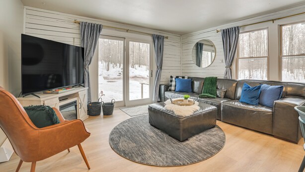A modern living room with a large flat-screen TV, leather sofas, a coffee table, and a fireplace. - 22 Mi to Boyne Mountain: Home w/ Fire Pit! (Petoskey)