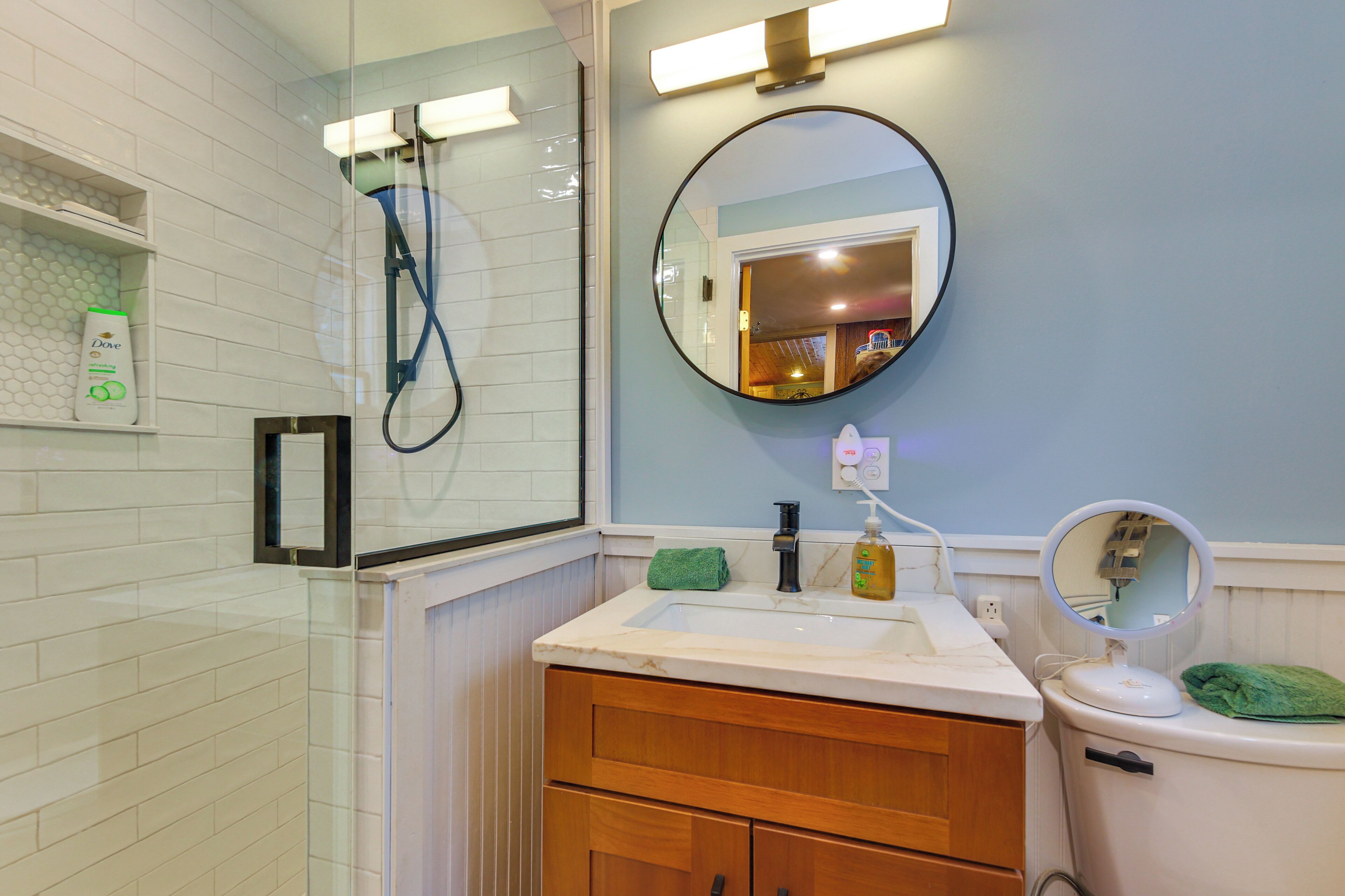 Un bagno con cabina doccia in vetro, lavandino con specchio e WC.