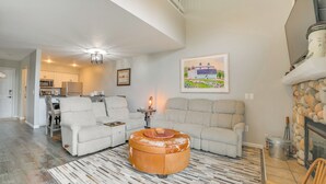 Un salon comprenant un canapé d’angle, un pouf rond et un tapis à motifs. On y trouve une cheminée avec un manteau en pierre et un tableau encadré accroché au mur.