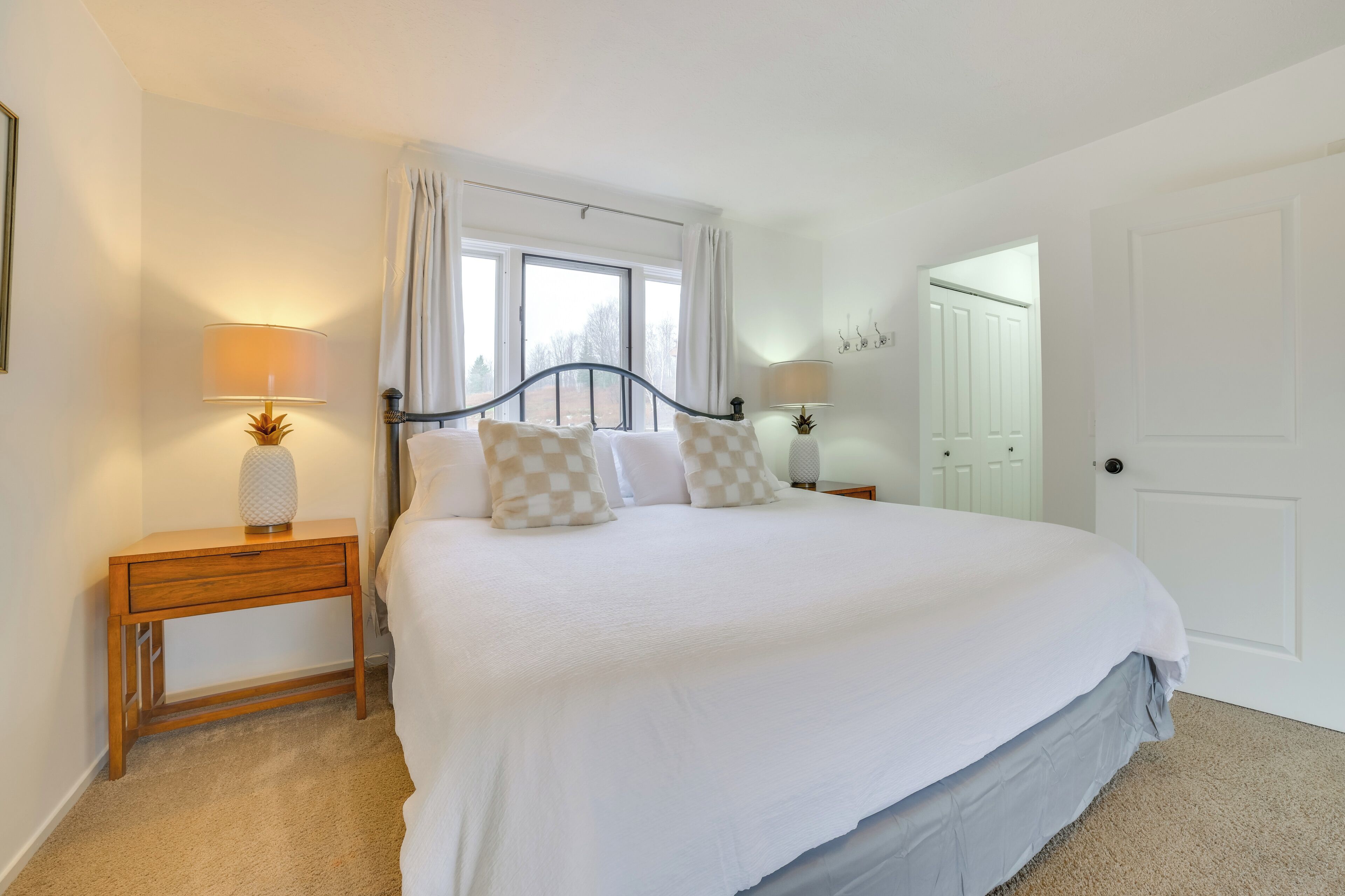A neatly made bed with a checkered pillow, two bedside lamps, and a window with curtains.