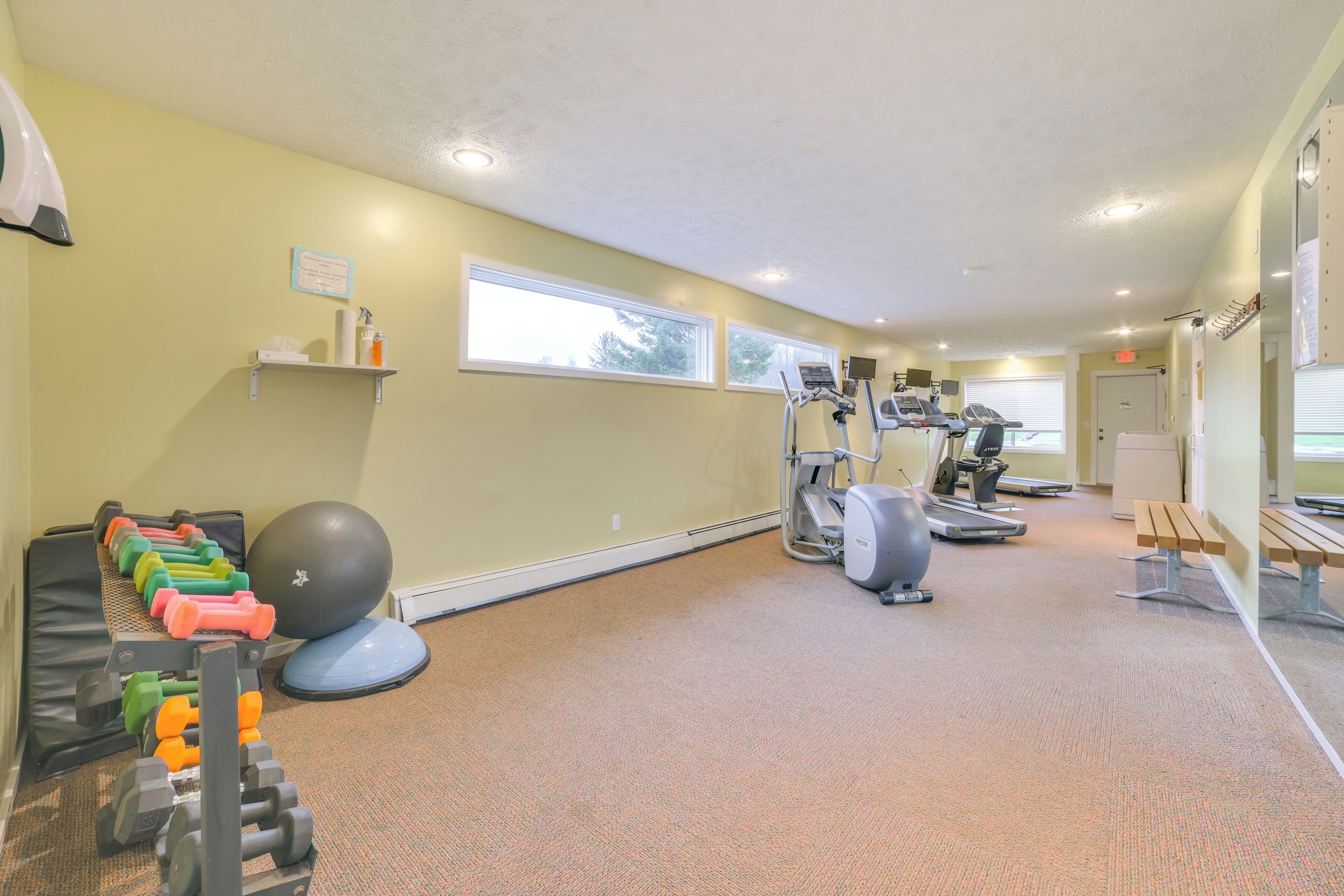 A gym with exercise equipment, a wall-mounted shelf with towels, and a window providing natural light.