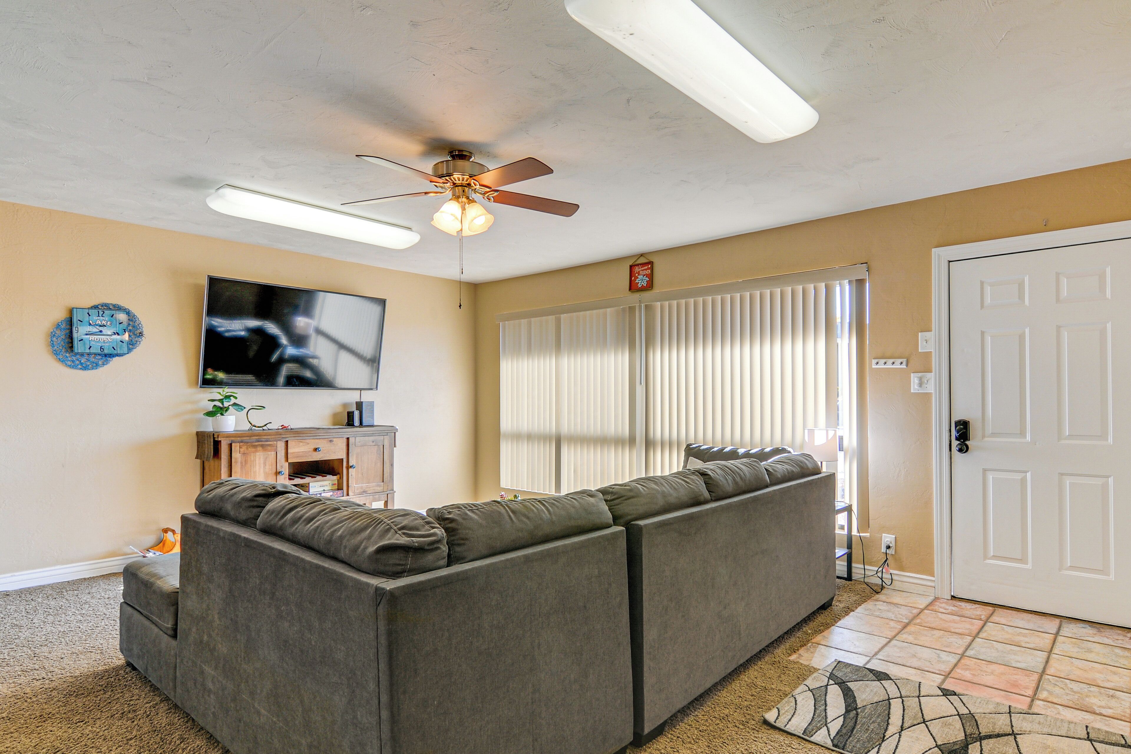 A living room with a sectional sofa, a ceiling fan, a flat-screen TV, and a door with a keypad lock.