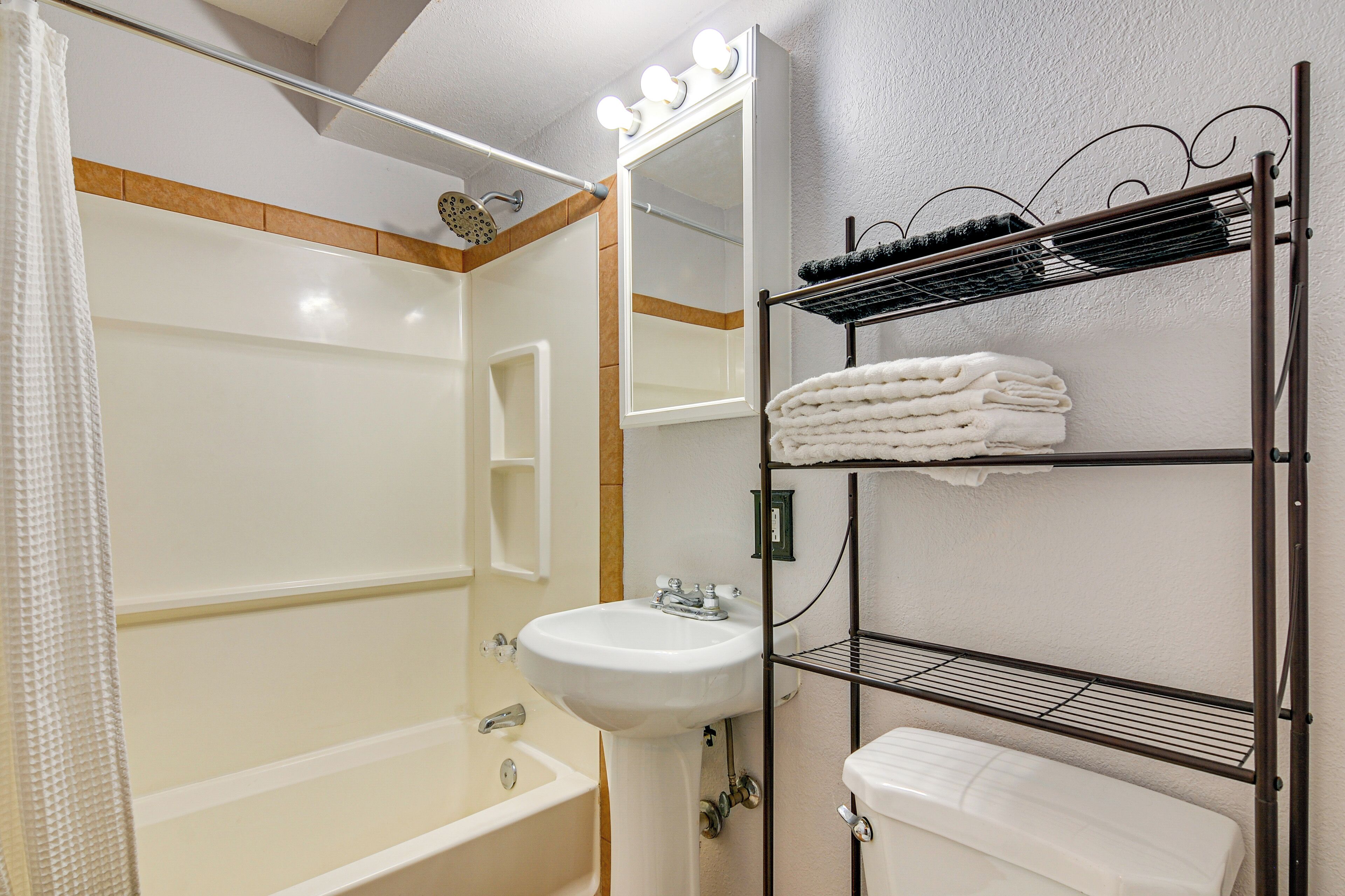 A bathroom with a bathtub, a sink, and a mirror with lights above.