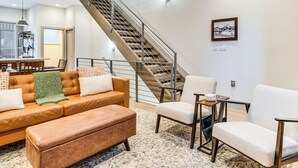Una sala de estar moderna con una escalera, un sofá de cuero, sillones y un comedor.