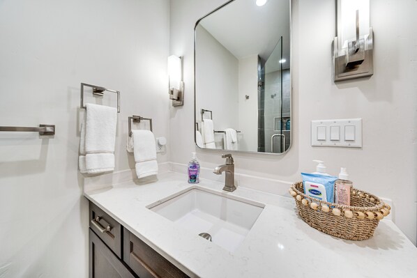 Un baño moderno con un espejo grande, dos toalleros, un lavabo y una cesta de mimbre con artículos de aseo.