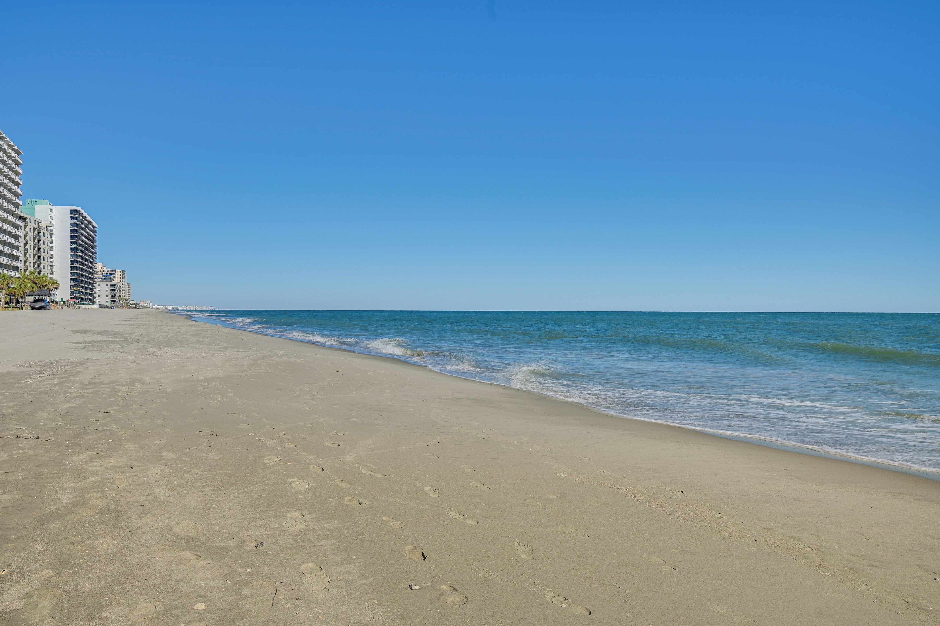 A beach with a clear sky, sandy shore, and high-rise buildings in the background.