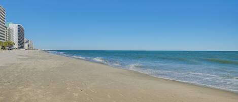 A beach with a clear sky, sandy shore, and high-rise buildings in the background.